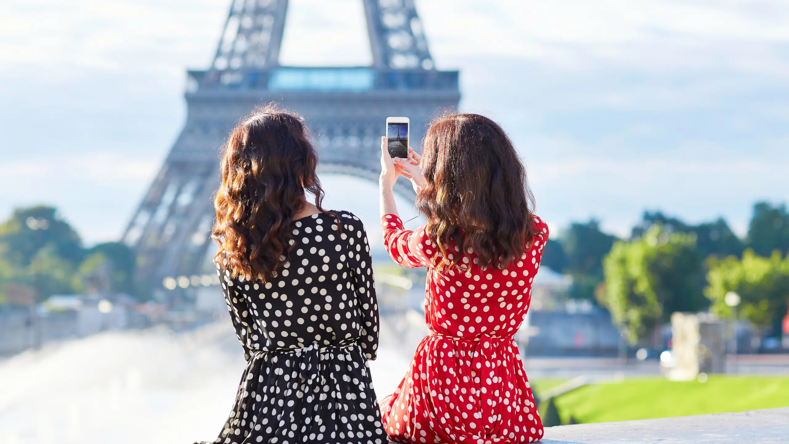 Zwei Frauen mit Pünktchenkleidern, die vor dem Eiffelturm in Paris sitzen
